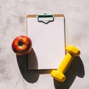 Flat lay of apple, clipboard, and dumbbell representing fitness and nutrition concept.